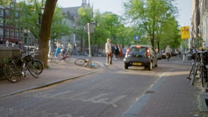 Blurred people and bicycles in a scenic european city street with cars and trees creating a vibrant urban atmosphere on a sunny day.