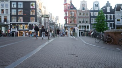 Blurred pedestrians walking along a cobblestone street in amsterdam with iconic narrow houses and bicycles, creating a classic bokeh cityscape in the netherlands.
