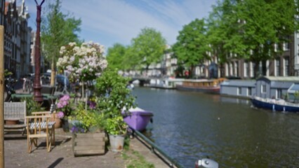 Fototapeta premium Blurred canal scene in amsterdam with defocused greenery and historic buildings creating a serene and picturesque bokeh effect along the netherlands waterways.