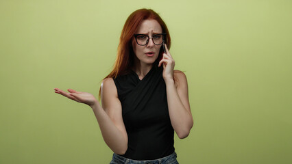 Woman with glasses and red hair on phone against a yellow wall showing frustration and confusion...