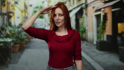 Woman saluting on a lively city street with vibrant buildings and plants, showcasing fashion in a casual yet stylish red top, surrounded by urban scenery and natural elements.