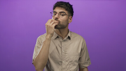 Hispanic man wearing glasses and beige shirt blowing kiss gesture with lips in purple studio; affection tenderness.