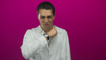 Young hispanic man in white shirt finger to throat for cutting and points finger in studio;...