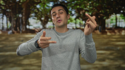 Young man laughing and flipping middle finger amid green trees in a sunlit park while grinning...