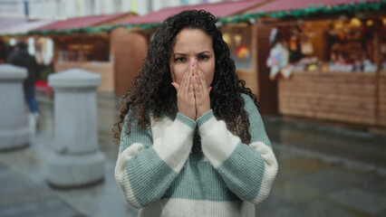 Woman sneezing in outdoor street market with wooden stalls, capturing a candid moment of allergy discomfort in a busy marketplace setting.