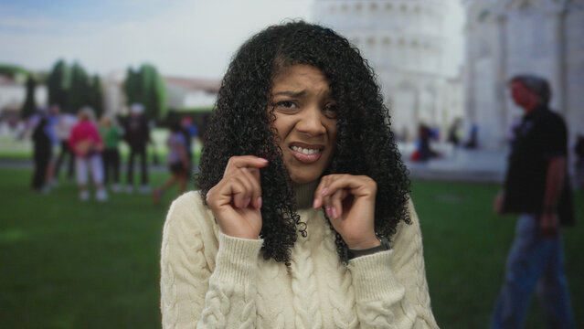 Woman raising hands by face at pisa tower landmark building in public square with blurred tourists; disgust.