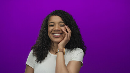 African american woman with hand on cheek laughing in purple studio wearing white t shirt;...