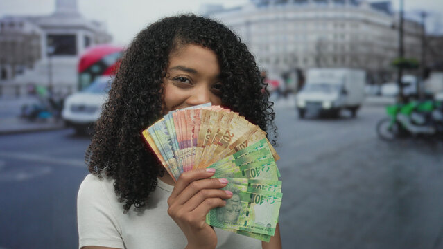 Woman smiling while holding rand banknotes on crowded city street in daylight; wealth ambition confidence.