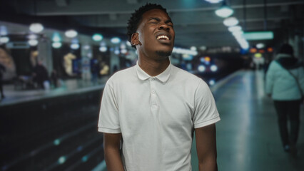 Fototapeta premium Man grimaces on empty train station platform wearing white polo shirt; frustration delay commute hurry.