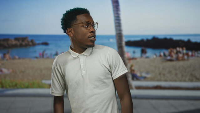 Man wearing glasses and white polo shirt standing on street in front of a blurred beach and leaning palm tree; serenity. - Powered by Adobe