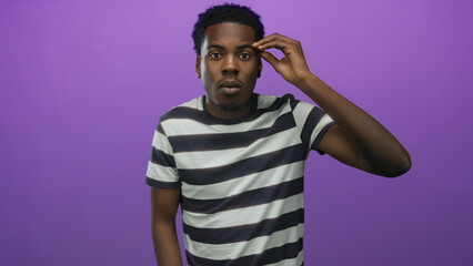 Man pinches thumb and index finger close together in a purple studio setting; precision contemplation.