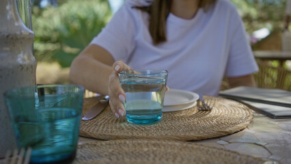 Woman pouring water into a glass at an outdoor mediterranean restaurant setting with wicker...