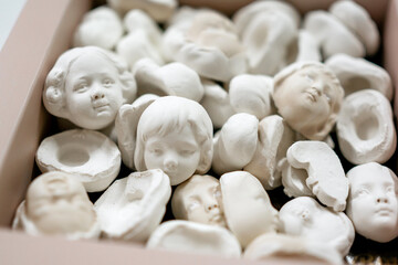 Close-up of a box filled with small white plaster doll heads for crafting and handmade vintage decorations