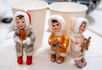 Trio of Hand-Painted Vintage-Style Christmas Ornament Figurines of Children in Winter Suits (Red, Orange, and Pink), Displayed with Teddy Bear and Deer Cutouts, Showcasing Nostalgic Holiday Craftsmans