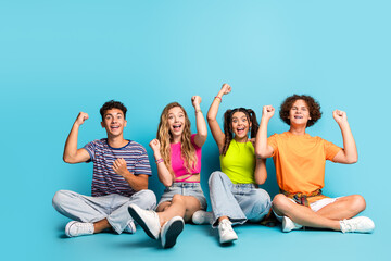 Obraz premium Group of four teens celebrate together on bright blue background full of energy and smiles