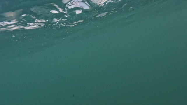 Half underwater perspective of sea with visible foam, bubbles and slow motion waves crossing the camera frame.