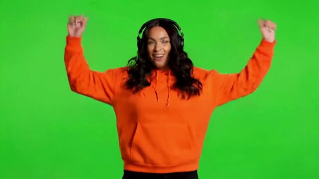 Joyful woman with headphones dancing enthusiastically, celebrating a win on a green screen background.