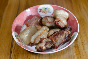 A bowl of traditionally smoked pork pieces with rich brown and golden fat layers, served in a floral-patterned dish.