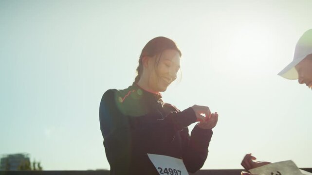 Two female athletes prepare for a race or marathon. One woman helps the other attach her bib number, symbolizing readiness and teamwork before a sporting event.