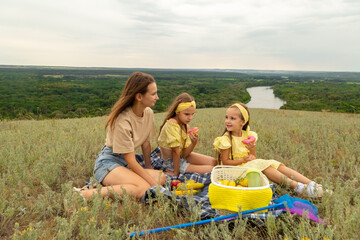 Mom and daughter enjoying picnic in nature, sitting on blanket on grass, eating donuts and having fun together