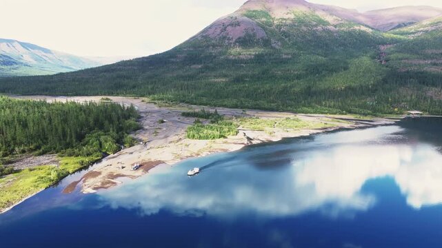 River mouth and delta sandbar reflect white cloud on calm Lake Lama within the Putorana Plateau. Base camp and tiny pier hint at access to a vast UNESCO wilderness in late summer daylight