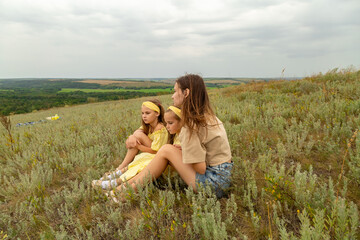 Fototapeta premium Happy mother and her children sitting together in field in nature outdoors relaxation
