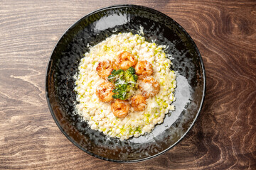 Gourmet shrimp risotto with corn, broccoli, and grated cheese served in a black bowl on rustic wood. Creamy texture, vibrant colors, and elegant plating ideal for food photography.