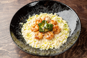 Gourmet shrimp risotto with corn, broccoli, and grated cheese served in a black bowl on rustic wood. Creamy texture, vibrant colors, and elegant plating ideal for food photography.