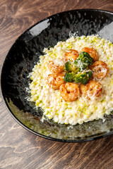 Gourmet shrimp risotto with corn, broccoli, and grated cheese served in a black bowl on rustic wood. Creamy texture, vibrant colors, and elegant plating ideal for food photography.