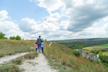 Fototapeta premium Father and daughter stand on top of hill and enjoy beautiful scenery of green hills under blue cloudy sky.