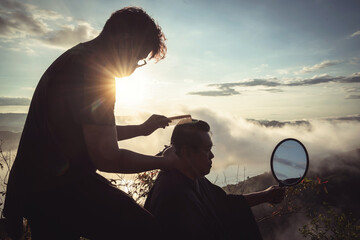 Hair styling in nature, man getting a haircut against a sunset backdrop, scenic view of mountains and clouds, outdoor grooming experience, personal care