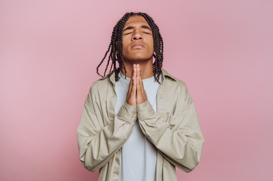 portrait of young man is seen with a prayerful pose, conveying a sense of hopefulness on pink background