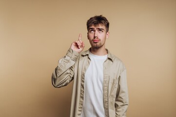 portrait of young thoughtful man points upwards, suggesting an idea or realization on beige background