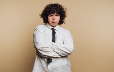 portrait of young woman in a white shirt and tie shows a frustrated expression, embodying a moment of discontent on beige background
