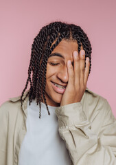 portrait of young man covers his face with his hand, expressing shyness and vulnerability on pink...