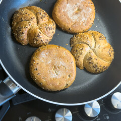 Fresh whole grain bread rolls with seeds warming in a non-stick frying pan on a stove. Close-up of crispy multigrain buns.