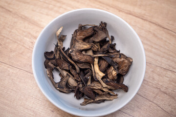 Dried bolete mushrooms in a light brown bowl on a wooden table. Natural dehydrated wild mushrooms prepared for cooking and seasoning.