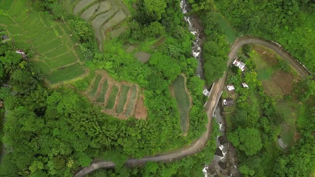 A wide aerial angle arcs in a slow half-circle over terraced fields and a winding stream. Scattered buildings and dense forest settle into view as whitewater threads through the vibrant hillside.