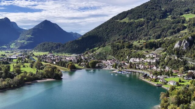 The small town of Walenstadt and its harbor nestle on the shore of the turquoise Walensee beneath steep, forested Swiss Alpine slopes. Concept of sheltered Alpine habitation.