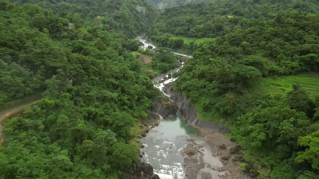 A wide aerial angle drifts to a final hold over mist-covered peaks and a winding river. Dense forest blankets the valley as rocky terrain and steep slopes settle into the layered landscape.