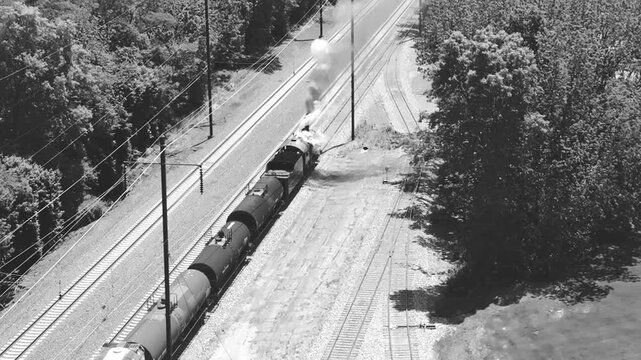 A steam freight train moves along the railway, releasing clouds of smoke as it travels through green landscapes. Creating a nostalgic scene of rail travel. In Black and White
