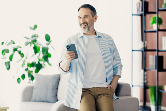 Professional mature man using smartphone in a stylish home office setting with a confident and engaged demeanor