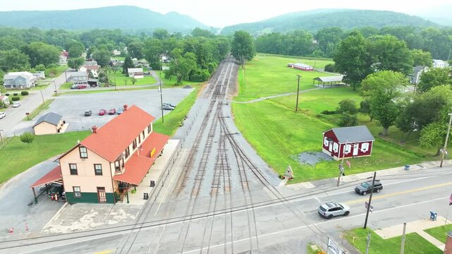 Trains meet at a crossroads in a scenic rural area. The view shows tracks winding through green hills and quaint buildings. This peaceful landscape captures the charm of small town life.