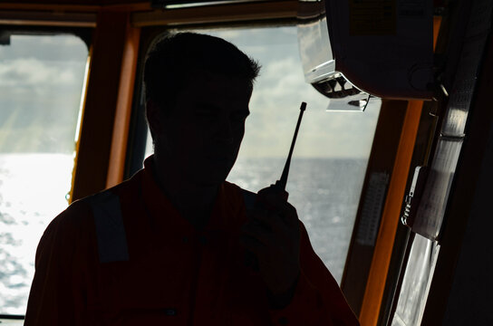 The duty officer of the offshore support vessel is talking with deck crew by a radio. The radio is used to ensure communication between the deck crew, bridge and the engine room crew