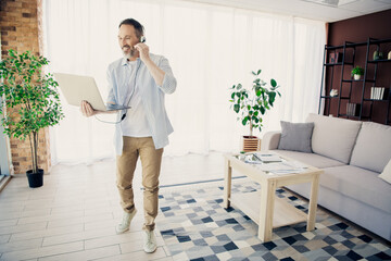 Professional man with headphones working on laptop at home office in stylish interior with natural decor