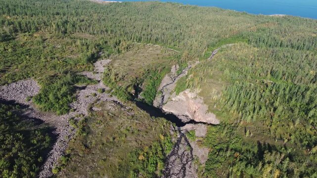 Sunny summer afternoon over a deep basalt canyon with a natural rock arch and dark stream, close to Lake Lama on the remote Putorana Plateau in Siberia. Pristine wilderness and dramatic geology create