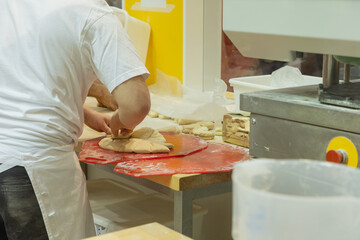 Baker preparing dough on red countertop commercial kitchen with various baking