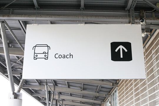 Coach bus direction sign hanging at terminal. Simple black and white transport symbol pointing the way to station area. Concept of navigation, orientation and travel guidance.