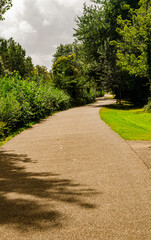 Winding path in a public park lined with trees and bushes and a cloudy sky