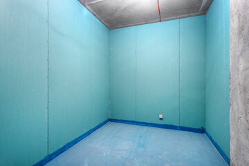 An empty room with waterproofed walls and floor before tiling.